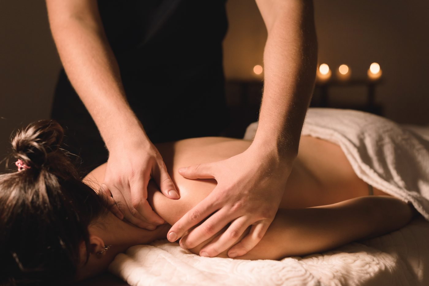 Professional massage therapist performing therapeutic massage on client's back in candlelit spa setting