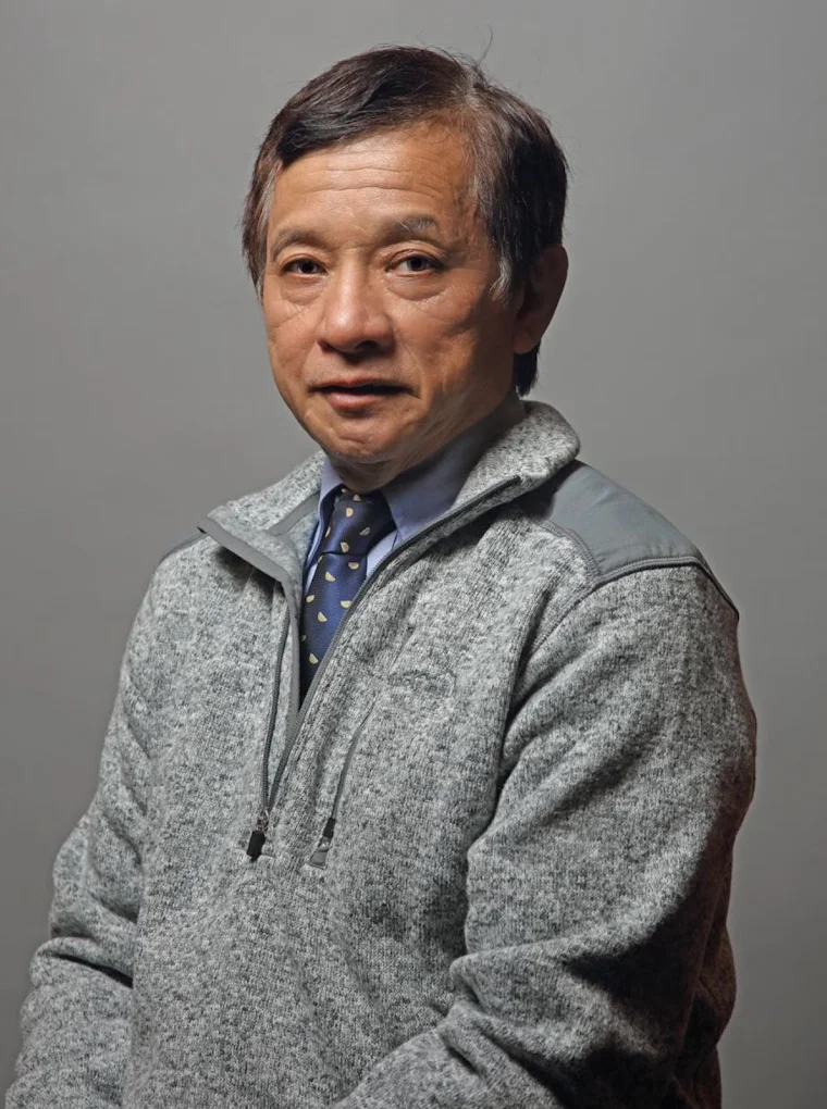 Middle-aged man wearing gray fleece jacket and blue dotted tie against neutral gray background