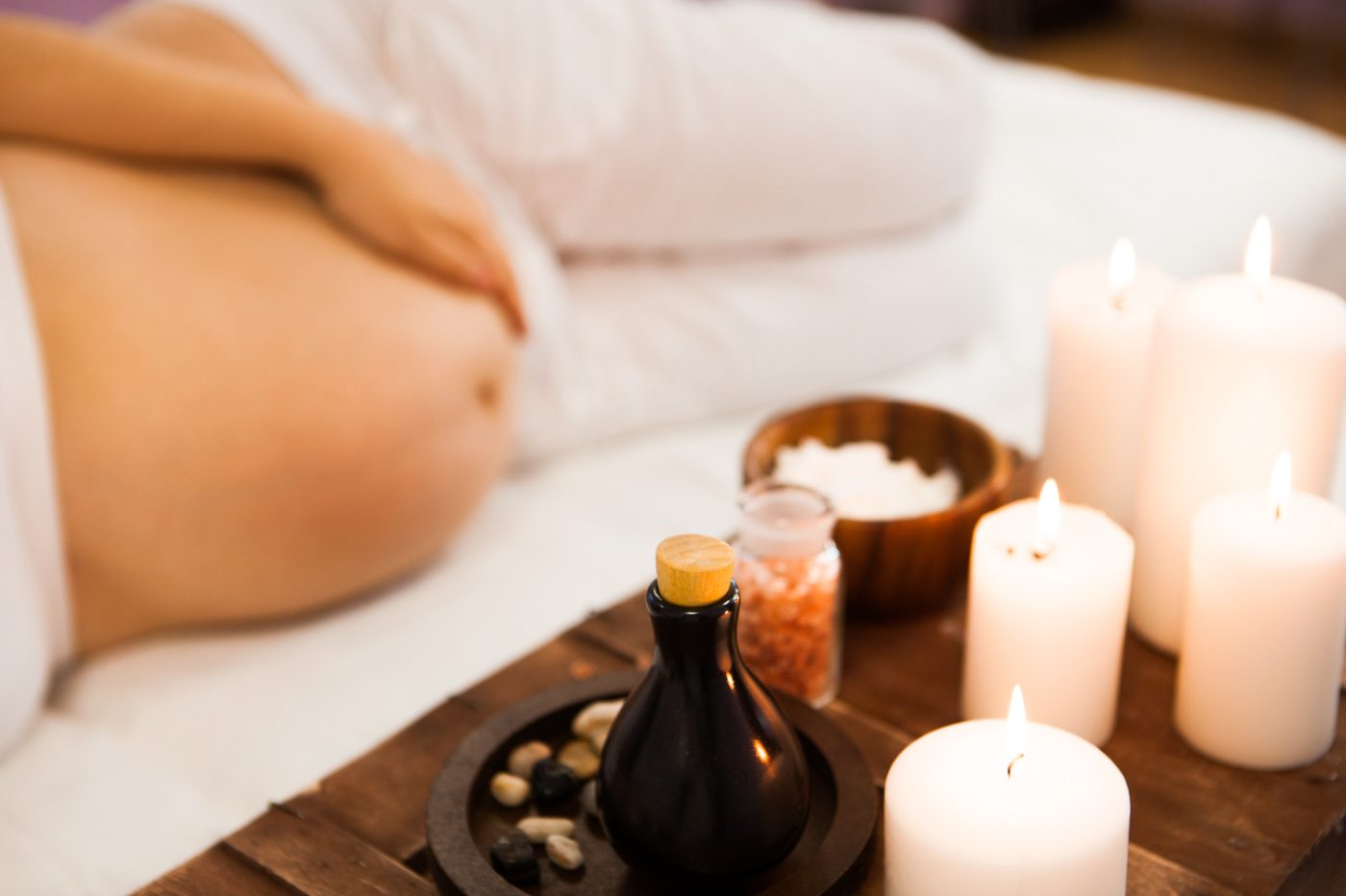 Spa setting with essential oil bottle, lit candles, salt bowl, and towels on wooden tray